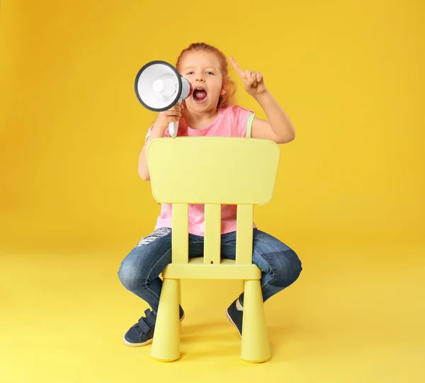 Linda niña con megáfono sentado en la silla contra el fondo de color — Foto de Stock