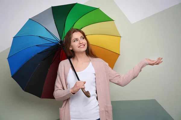 Giovane donna con ombrello arcobaleno su sfondo colore — Foto Stock