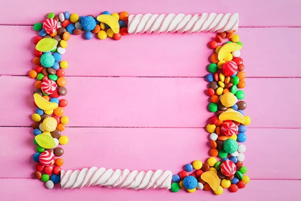 Рамка з різнокольорових цукерок на дерев'яному фоні, плоска — стокове фото