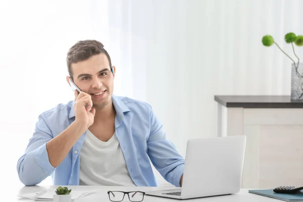 Jeune homme parlant au téléphone tout en travaillant avec ordinateur portable dans le bureau à la maison — Photo