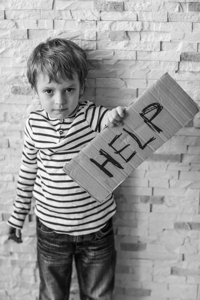 Hemlösa stackars pojken håller kartong med word hjälp nära tegelvägg — Stockfoto