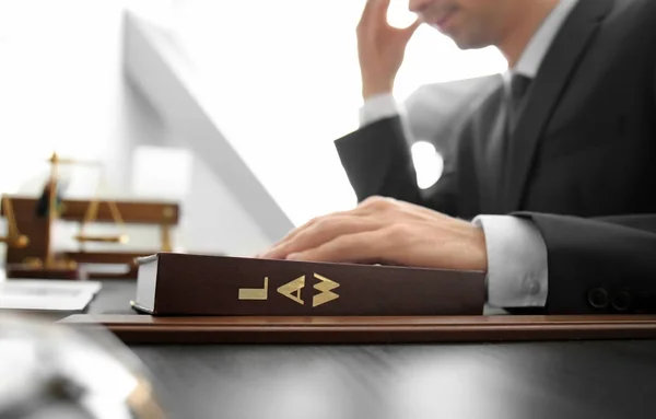 Lawyer holding hand on juridical textbook at table in office — Stock Photo, Image