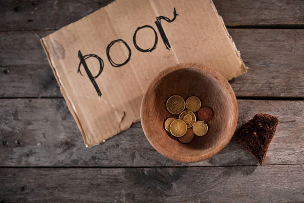 Coins and piece of cardboard with word POOR on wooden background — Stock Photo, Image