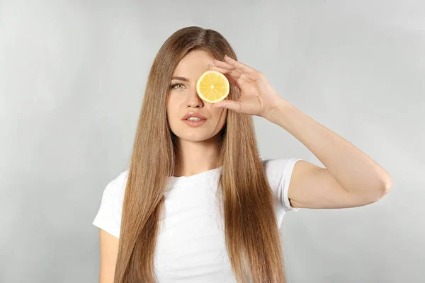 Schöne junge Frau mit einer Scheibe reifer Zitrone auf grauem Hintergrund — Stockfoto