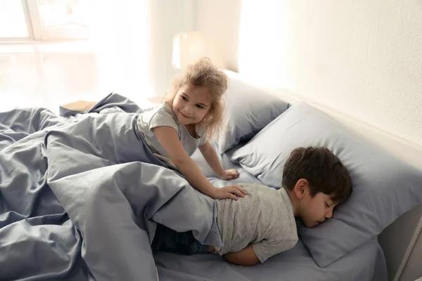 Söt liten flicka vaknar upp hennes bror på sängen hemma — Stockfoto