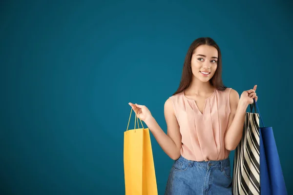 Schöne junge Frau mit Einkaufstaschen auf farbigem Hintergrund — Stockfoto