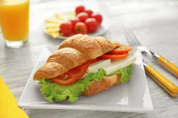 Тарелка с вкусным бутербродом с круассаном на столе — стоковое фото