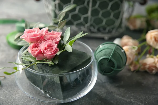 Glasskål med blommor i svampen på bord — Stockfoto