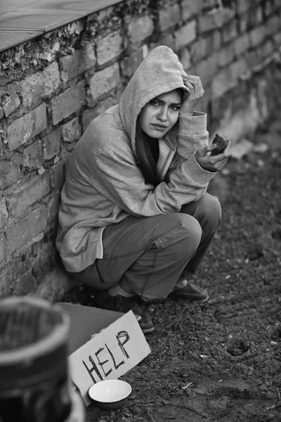 Бездомна бідна жінка сидить на відкритому повітрі біля шматка картону зі словом HELP — стокове фото