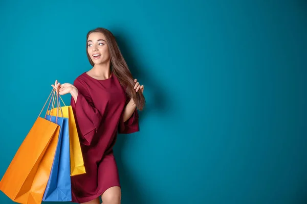 Mooie jonge vrouw met boodschappentassen op kleur achtergrond — Stockfoto