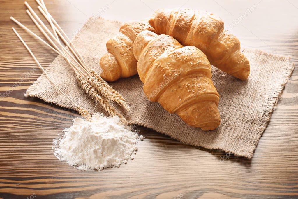 Tasty croissant, spikes and flour on table