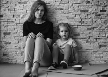 Homeless poor woman with little daughter sitting near brick wall clipart