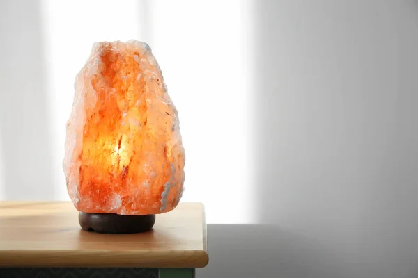 Himalayan salt lamp on wooden cabinet against light background