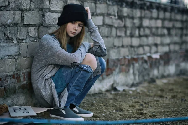 Homeless poor teenage girl sitting near brick wall outdoors — Stock Photo, Image