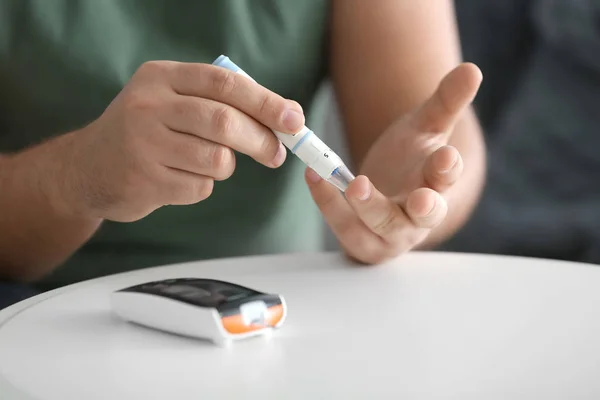 Diabetic man taking blood sample with lancet pen at home, closeup — Stock Photo, Image