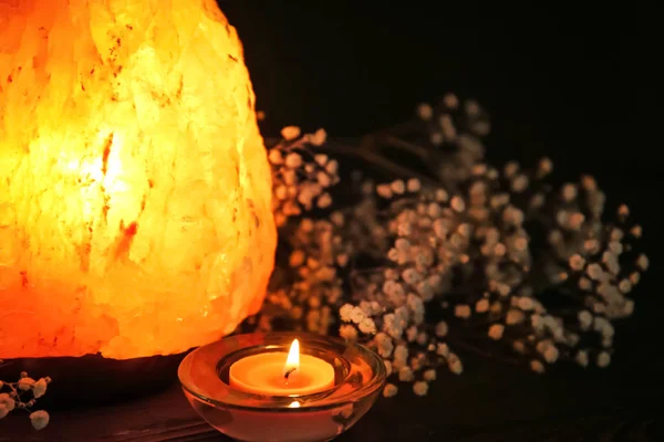 Lámpara de sal del Himalaya, velas y flores sobre la mesa sobre fondo oscuro —  Fotos de Stock