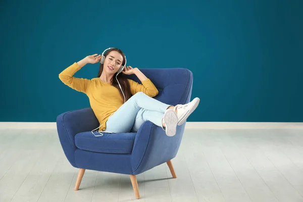 Красива молода жінка слухає музику, сидячи в зручному кріслі на кольоровій стіні — стокове фото