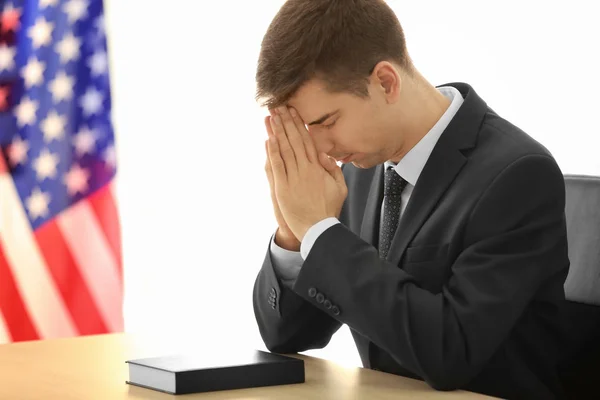 Młody człowiek modli się przy stole w pobliżu Flaga Amerykańska — Zdjęcie stockowe