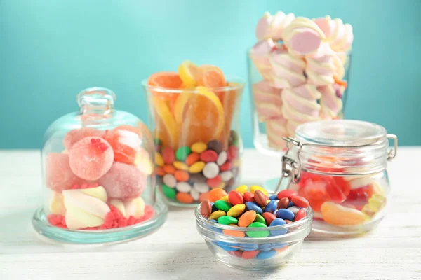 Louça de vidro com doces diferentes na mesa contra fundo de cor — Fotografia de Stock