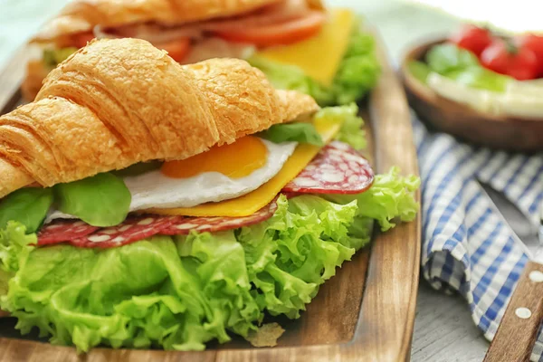 Holzbrett mit leckerem Croissant-Sandwich auf dem Tisch — Stockfoto