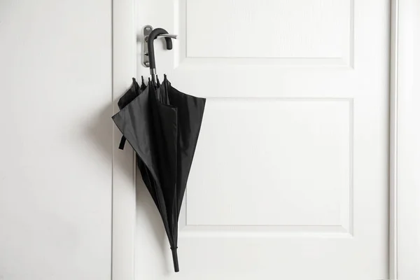 Black umbrella hanging on door indoors — Stock Photo, Image