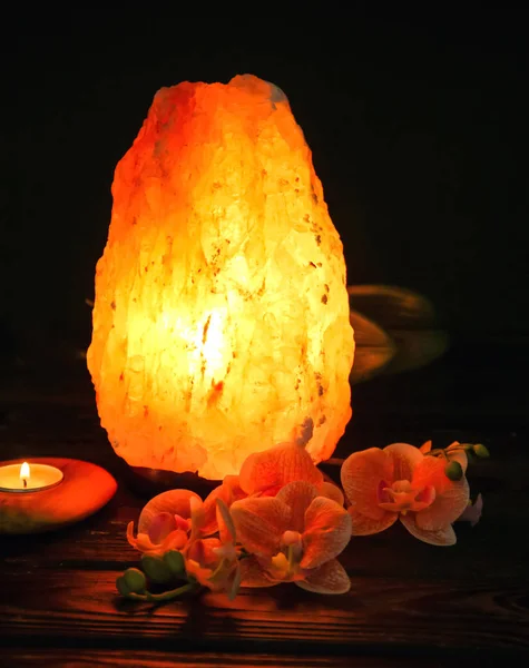 喜马拉雅盐灯 蜡烛和鲜花在桌子上反对黑暗背景 — 图库照片