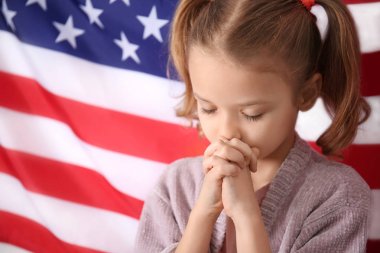 Cute little girl praying for America and flag on background clipart