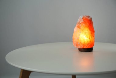 Himalayan salt lamp on table against light background clipart