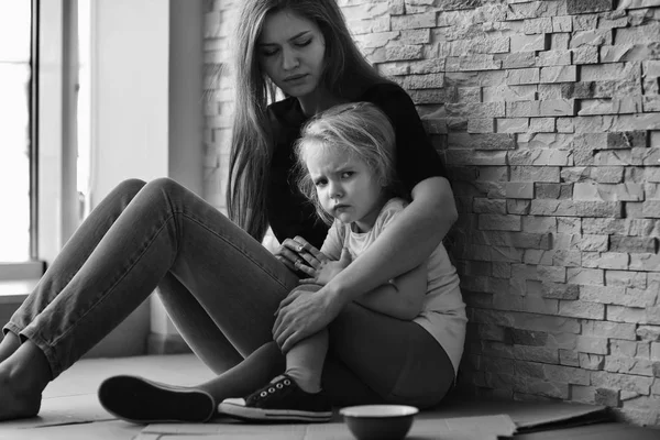 Homeless poor woman with little daughter sitting near brick wall