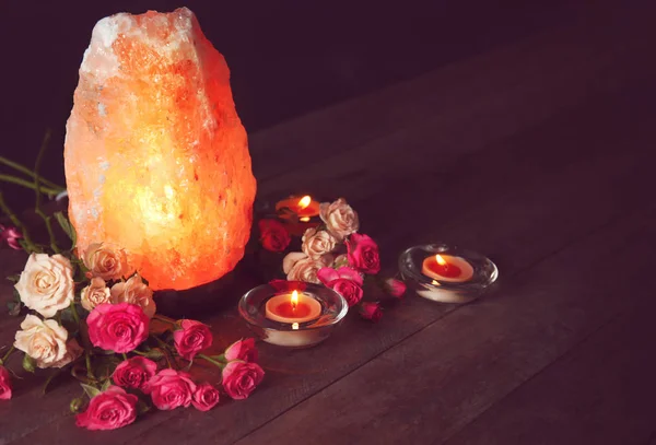 Гималайская соляная лампа, свечи и цветы на столе на тёмном фоне — стоковое фото