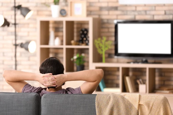 Uomo che guarda la TV mentre riposa sul divano di casa — Foto Stock