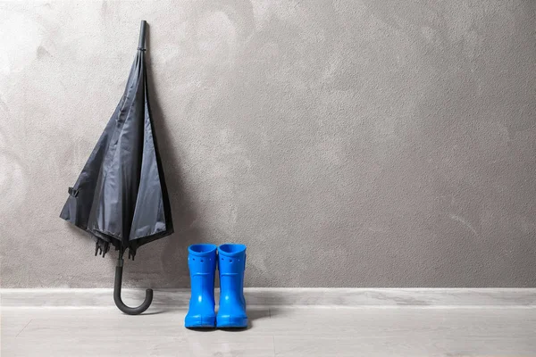 Black umbrella and gumboots on floor indoors — Stock Photo, Image