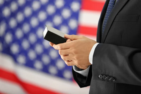 Hombre sosteniendo la Santa Biblia y la bandera americana en el fondo — Foto de Stock