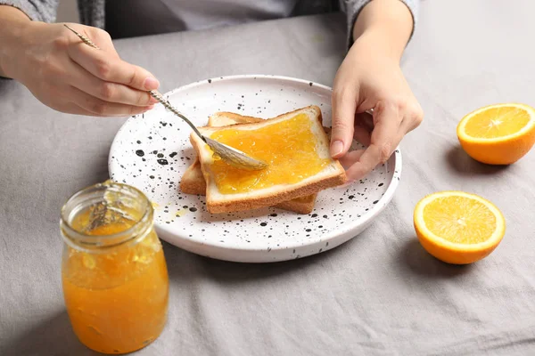 Wanita menyebarkan selai manis di atas roti panggang di meja — Stok Foto
