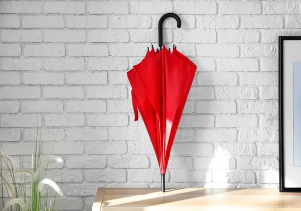 Elegante paraguas rojo en la mesa cerca de la pared de ladrillo — Foto de Stock