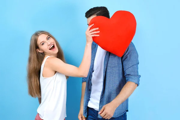 Giovane coppia tenendo cuscino a forma di cuore su sfondo chiaro — Foto Stock