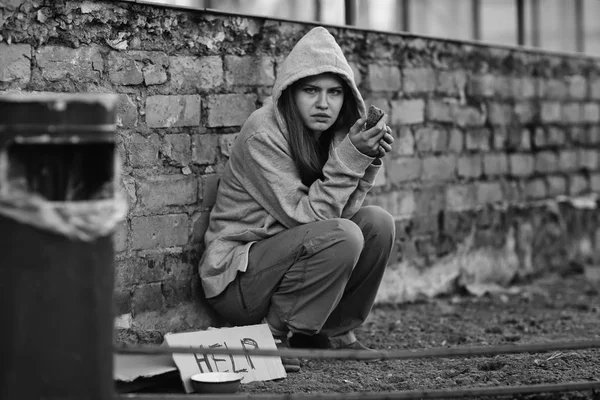 Homeless poor woman sitting outdoors near piece of cardboard with word HELP