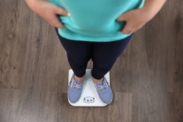 Overweight girl standing on floor scales indoors