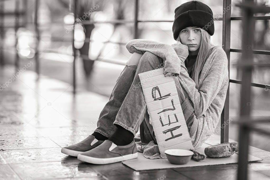 Homeless poor teenage girl holding piece of cardboard with word HELP outdoors