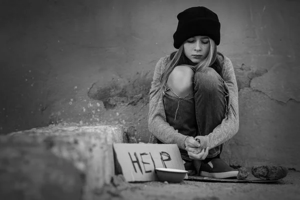 Бездомна бідна дівчина-підліток сидить на відкритому повітрі біля порожньої миски і шматка картону зі словом HELP — стокове фото
