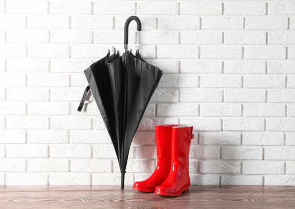 Parapluie noir et bottes de gomme près du mur de briques — Photo