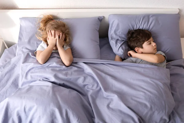 Lindo chico durmiendo mientras su hermana pequeña tratando de conciliar el sueño en la cama en casa. Hora de dormir familiar — Foto de Stock