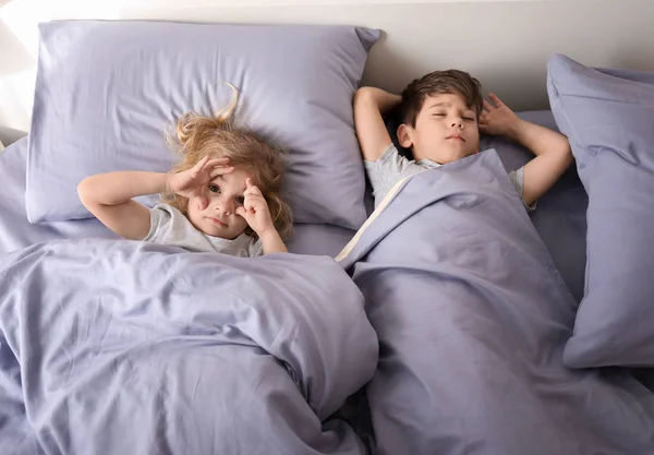 Lindo chico durmiendo mientras su hermana pequeña tratando de conciliar el sueño en la cama en casa. Hora de dormir familiar — Foto de Stock