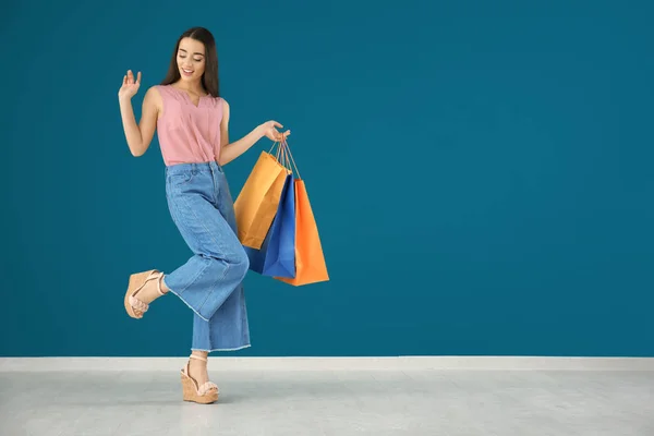 Hermosa mujer joven con bolsas de compras contra la pared de color —  Fotos de Stock