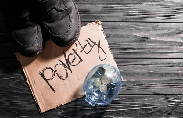 Old shoes, piece of cardboard with word POVERTY and piggy bank on wooden background — Stock Photo, Image