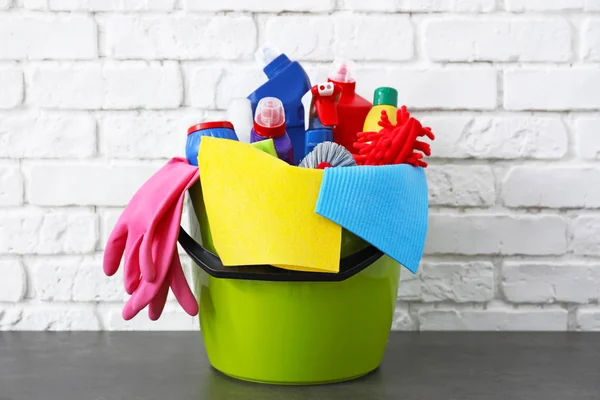 Bucket with cleaning supplies and tools on table near brick wall — Stock Photo, Image