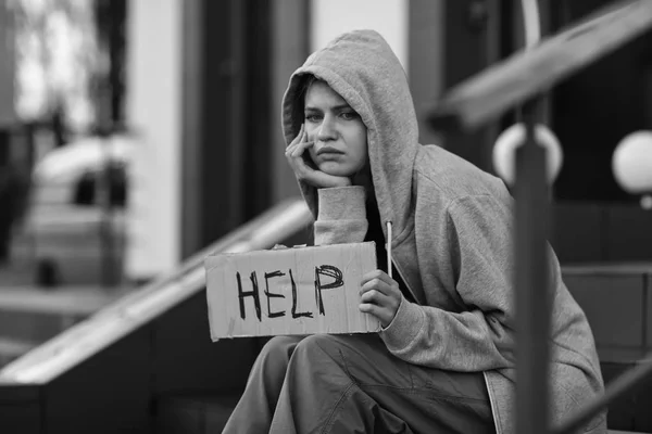 Povera donna senzatetto che tiene un pezzo di cartone con la parola AIUTO all'aperto — Foto Stock