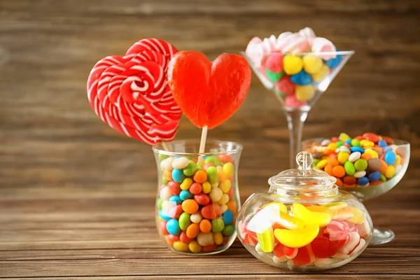 Artículos de vidrio con caramelos de colores sobre fondo de madera — Foto de Stock