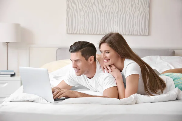 年轻夫妇与笔记本电脑在家里的床上 — 图库照片