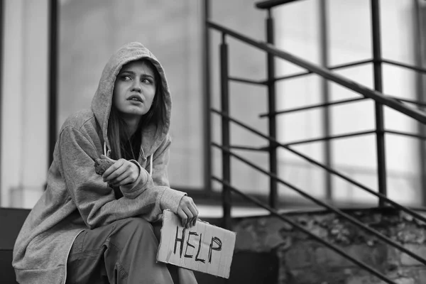 Povera donna senzatetto che tiene un pezzo di cartone con la parola AIUTO all'aperto — Foto Stock